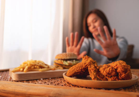 Woman declining fried chicken and fast food at table indoors.