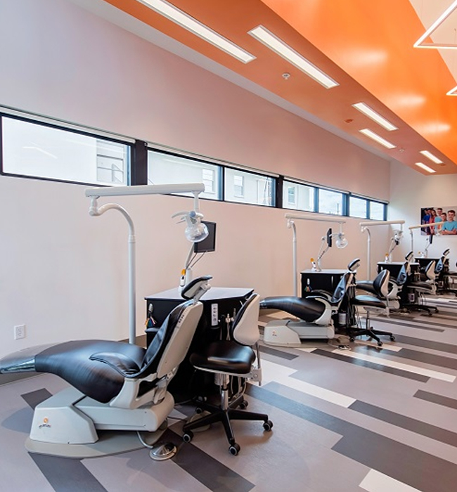Modern orthodontic office treatment room with dental chairs and equipment under orange ceiling lights.