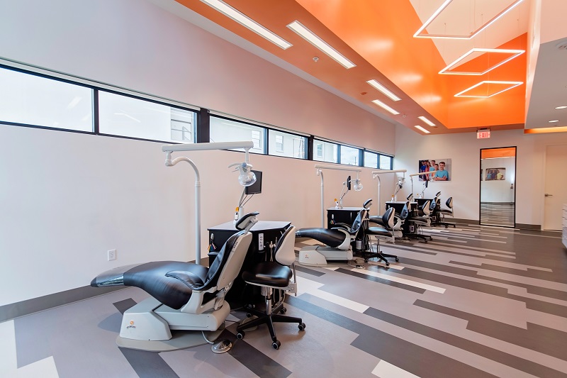 Modern orthodontic office interior with dental chairs, equipment, and bright orange ceiling lighting.