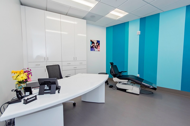 Modern orthodontic office reception area with white desk, turquoise accent wall, and waiting area.