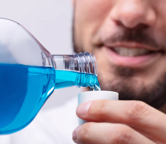 Man pouring blue mouthwash or rinse into a cup for oral hygiene care.