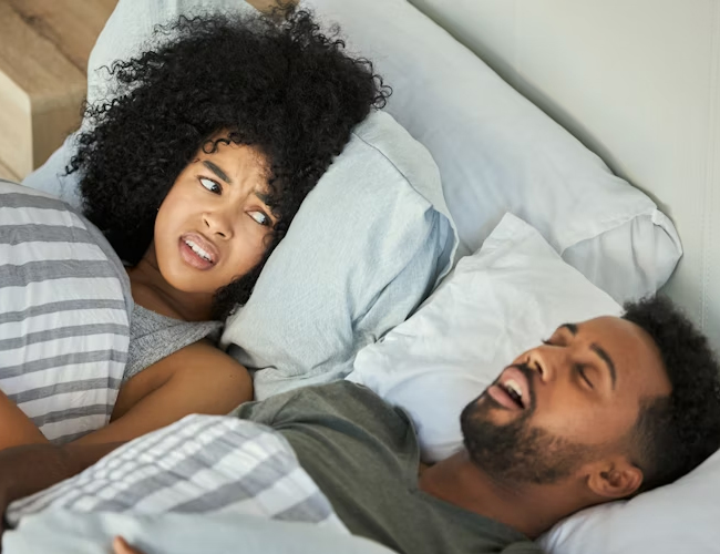 Couple lying in bed together, smiling and relaxed in bedroom setting.