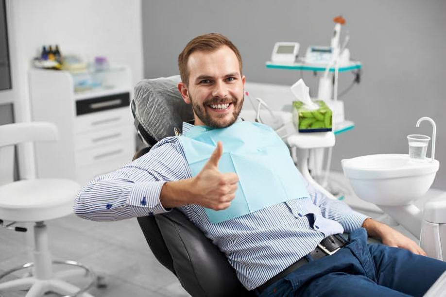 Smiling man giving thumbs up in modern dental office chair with orthodontic equipment visible.