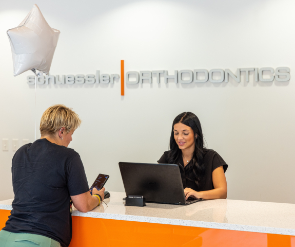 Woman consulting with orthodontist receptionist at orange desk in modern dental office.