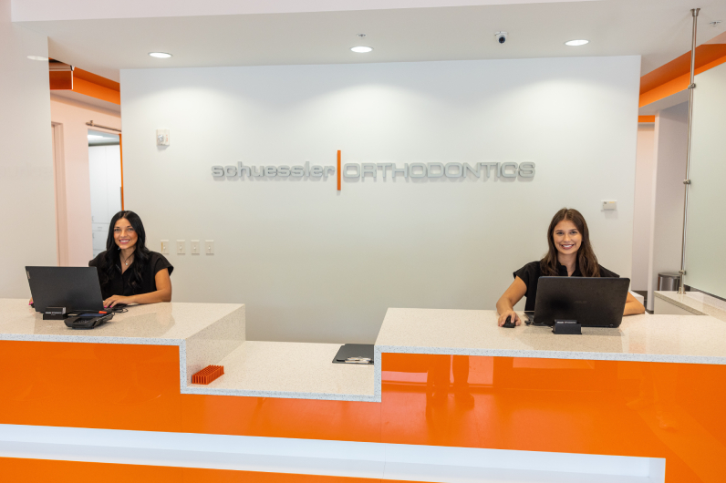 Two receptionists at modern orange and white orthodontic office front desk